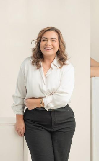 Bibiana Rojas sonriendo, con blusa blanca, apoyada en una repisa
